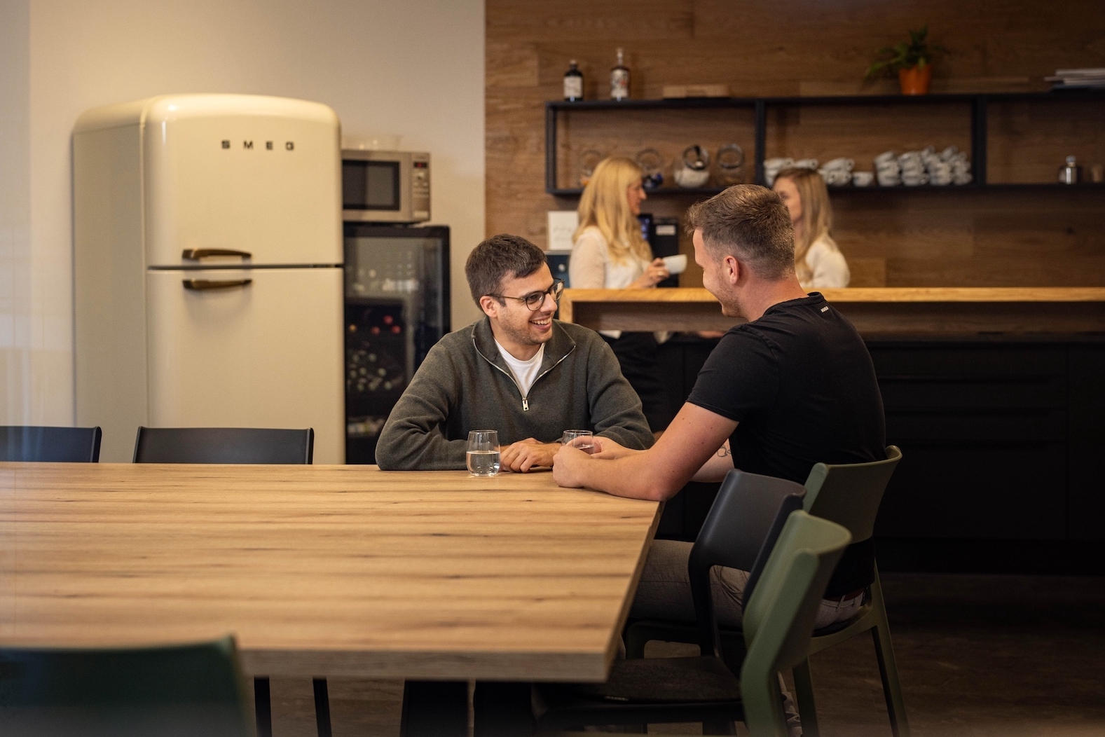 Zwei Mitarbeiter sitzen am Tisch in der Küche und diskutieren.